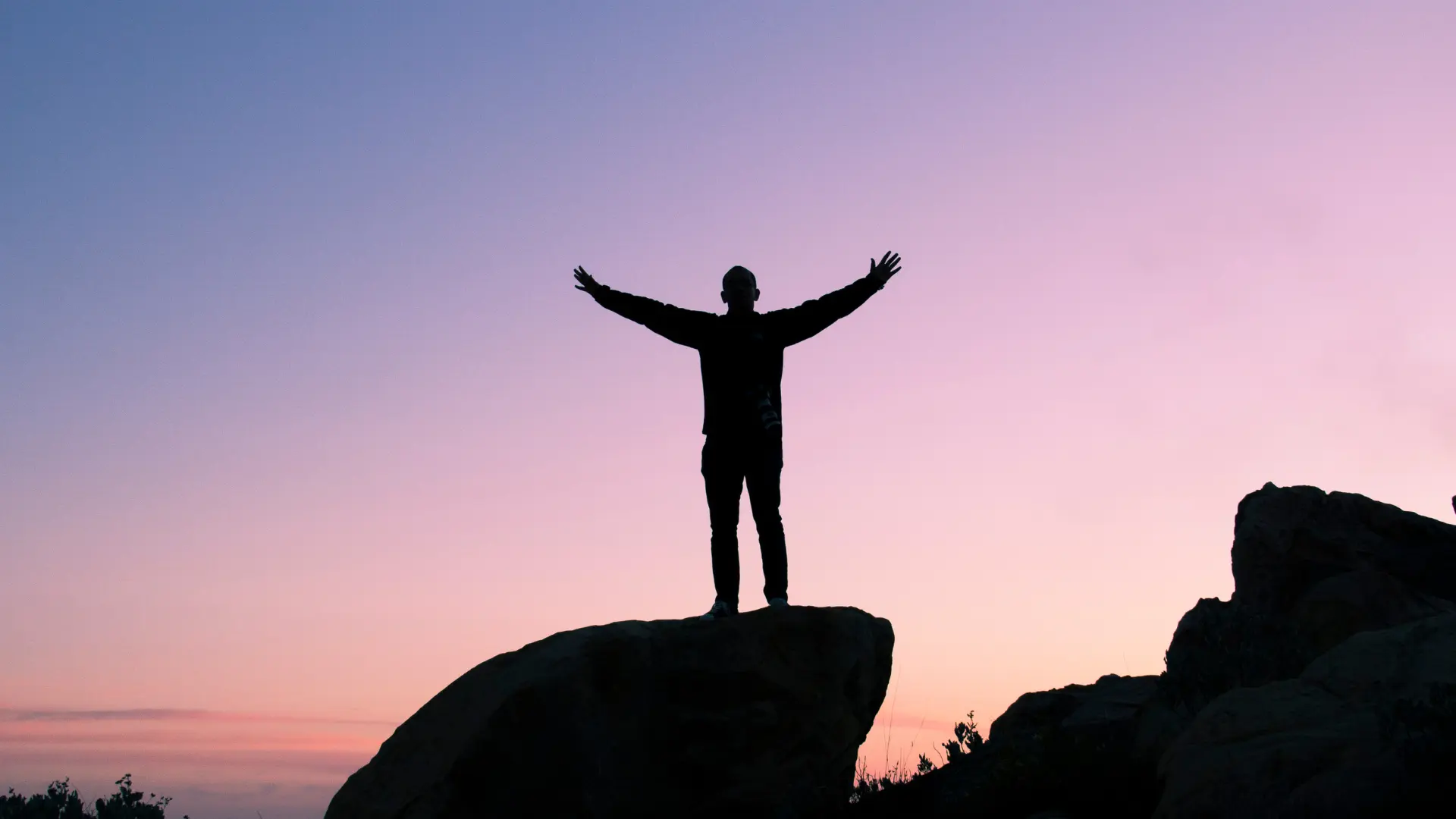 Person standing triumphantly on top of a rocky peak, arms raised towards the sky in a gesture of achievement and self-empowerment, with a backdrop of a clear horizon symbolizing clarity and personal growth.