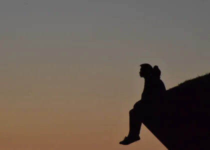 A person sitting on top of a large rock, gazing into the distance with a thoughtful expression, surrounded by a peaceful natural landscape. The scene reflects introspection, solitude, and emotional reflection.