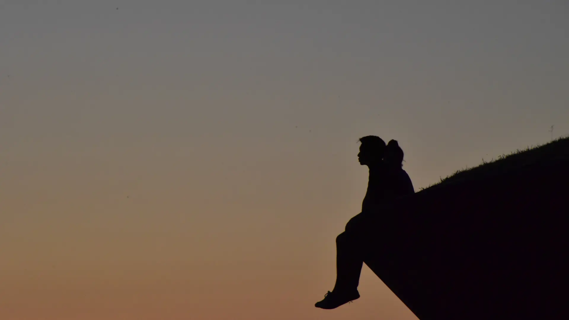 A person sitting on top of a large rock, gazing into the distance with a thoughtful expression, surrounded by a peaceful natural landscape. The scene reflects introspection, solitude, and emotional reflection.